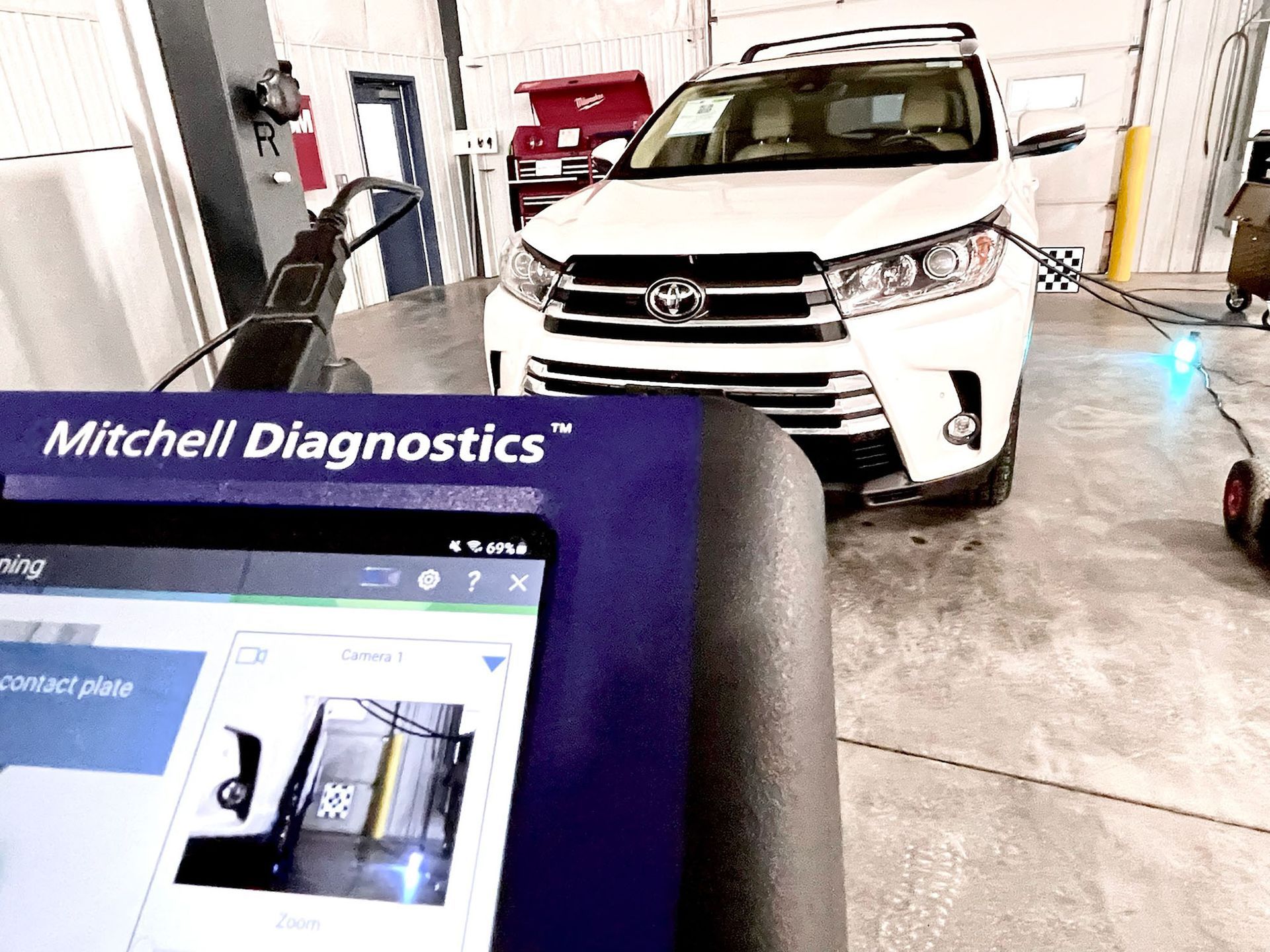A white toyota highlander is being tested by mitchell diagnostics in a garage.