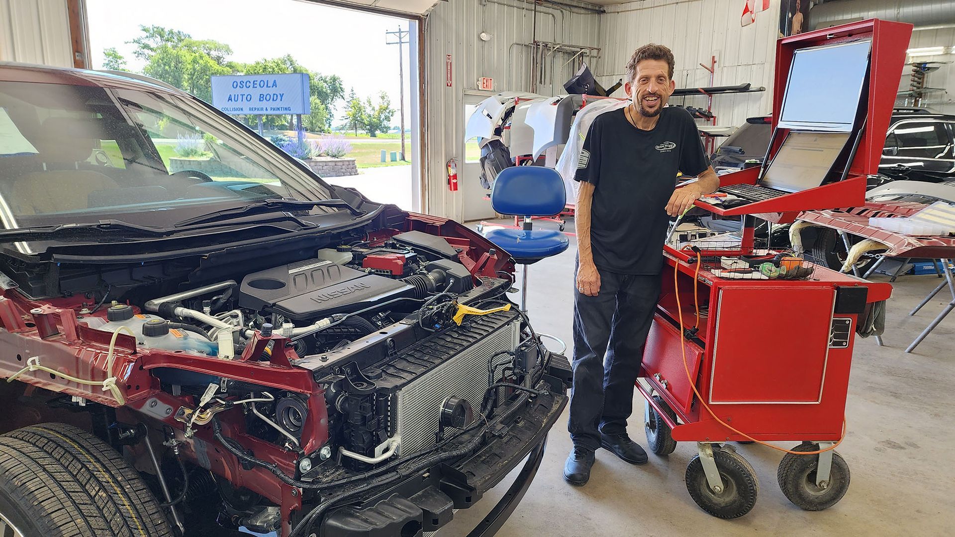A man is standing next to a car with the hood open in a garage.