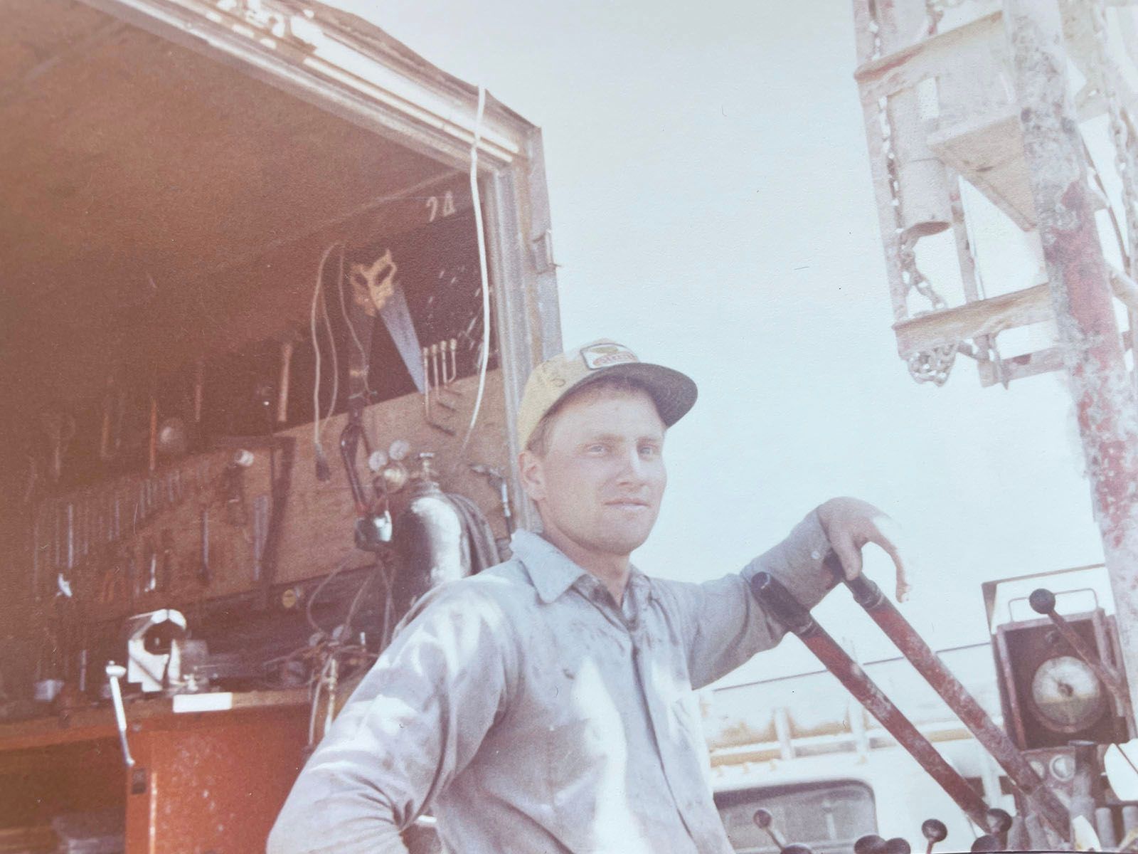 Man in a cap stands by a truck, holding a handle in an industrial setting