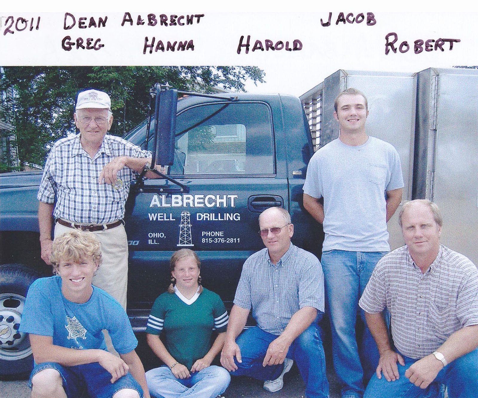 Six people posing beside a blue drilling truck