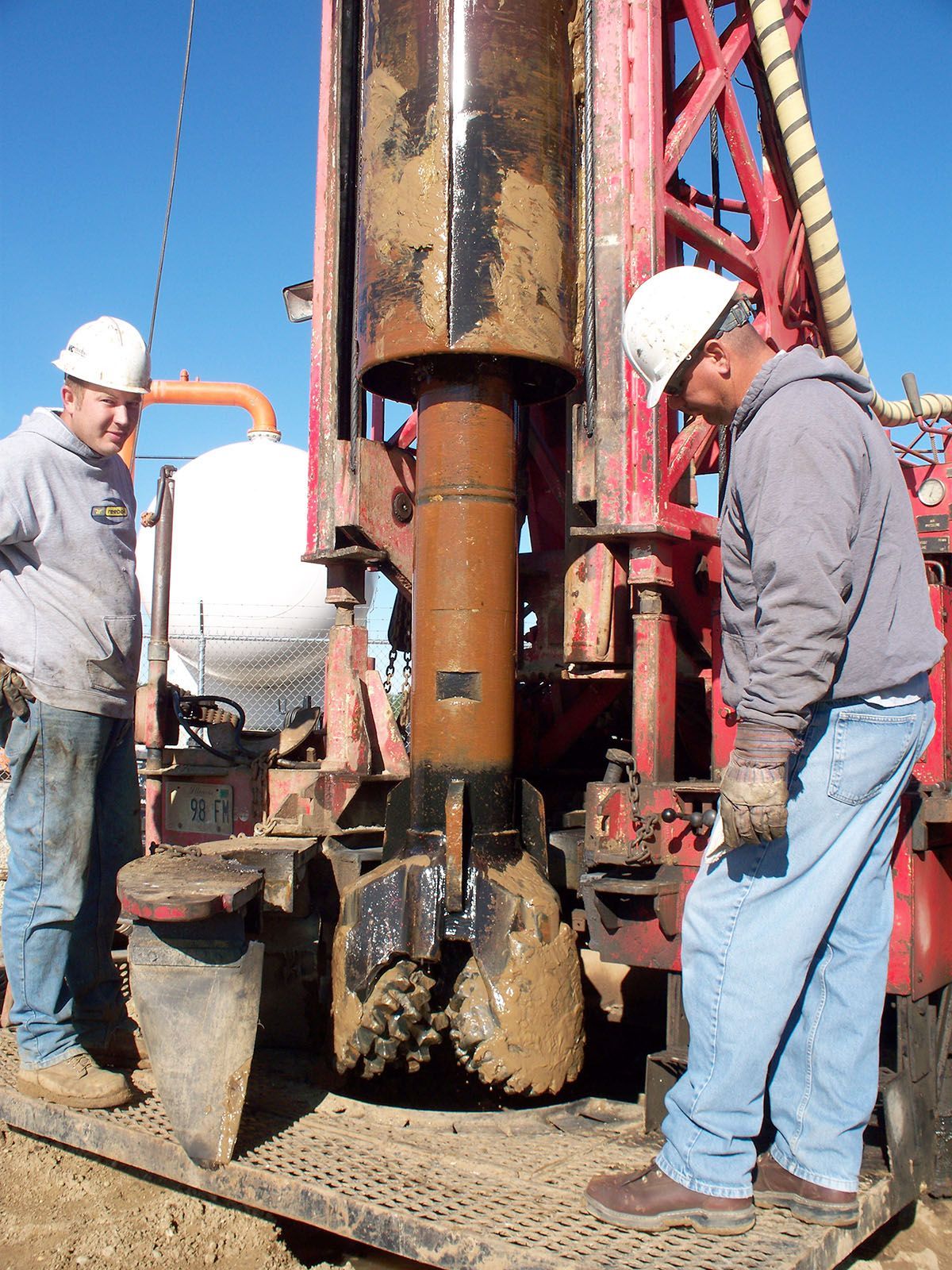 Workers in hard hats operating drilling equipment at an outdoor construction site