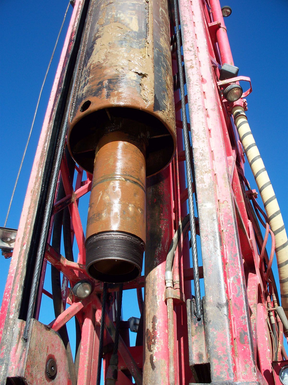 A drill pipe suspended in a red drilling rig