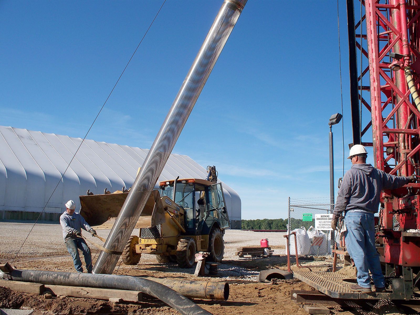 Construction workers guiding a large tilted pole at an outdoor worksite