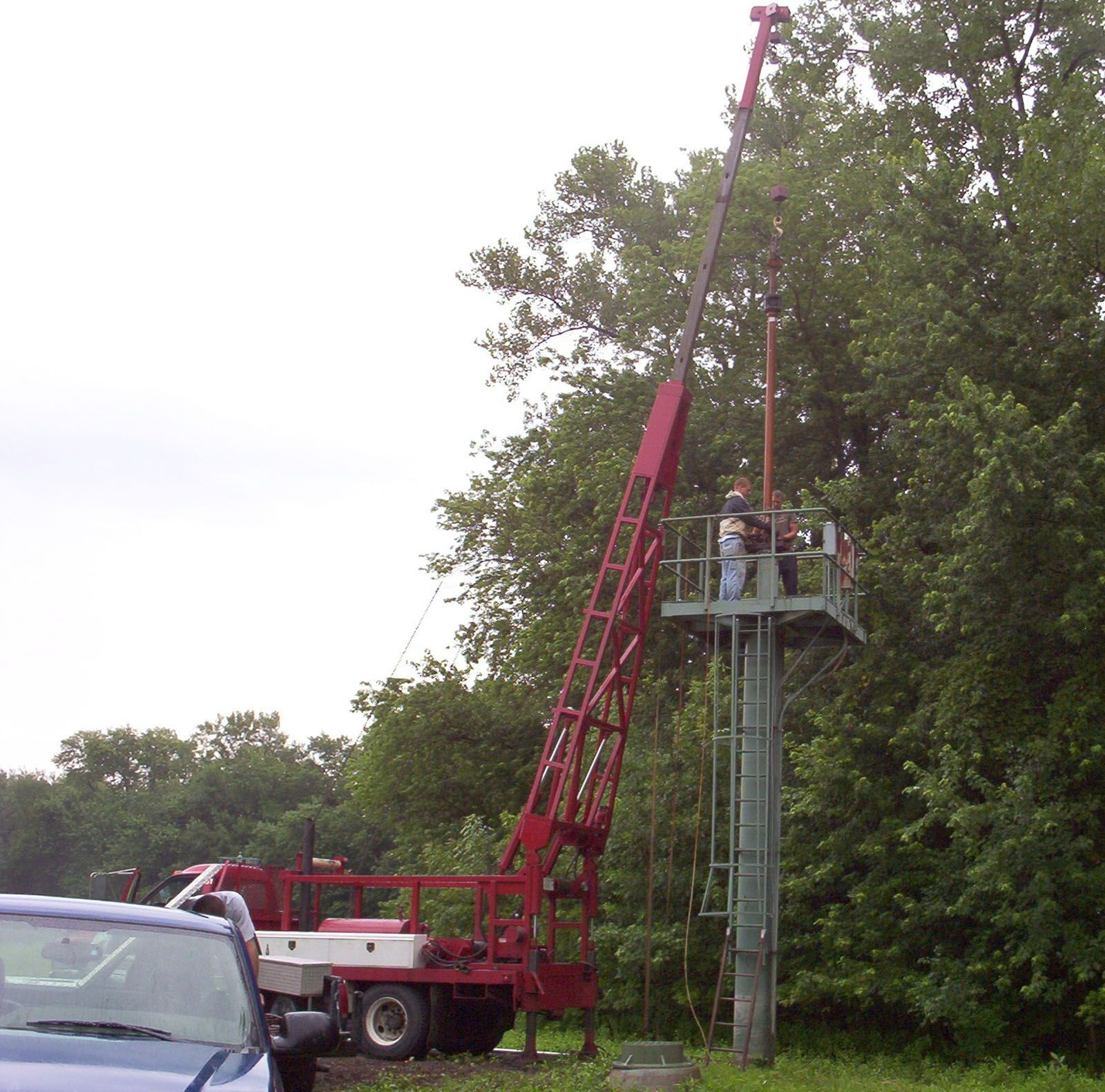 Red utility truck raising a worker on a platform beside a roadside tree