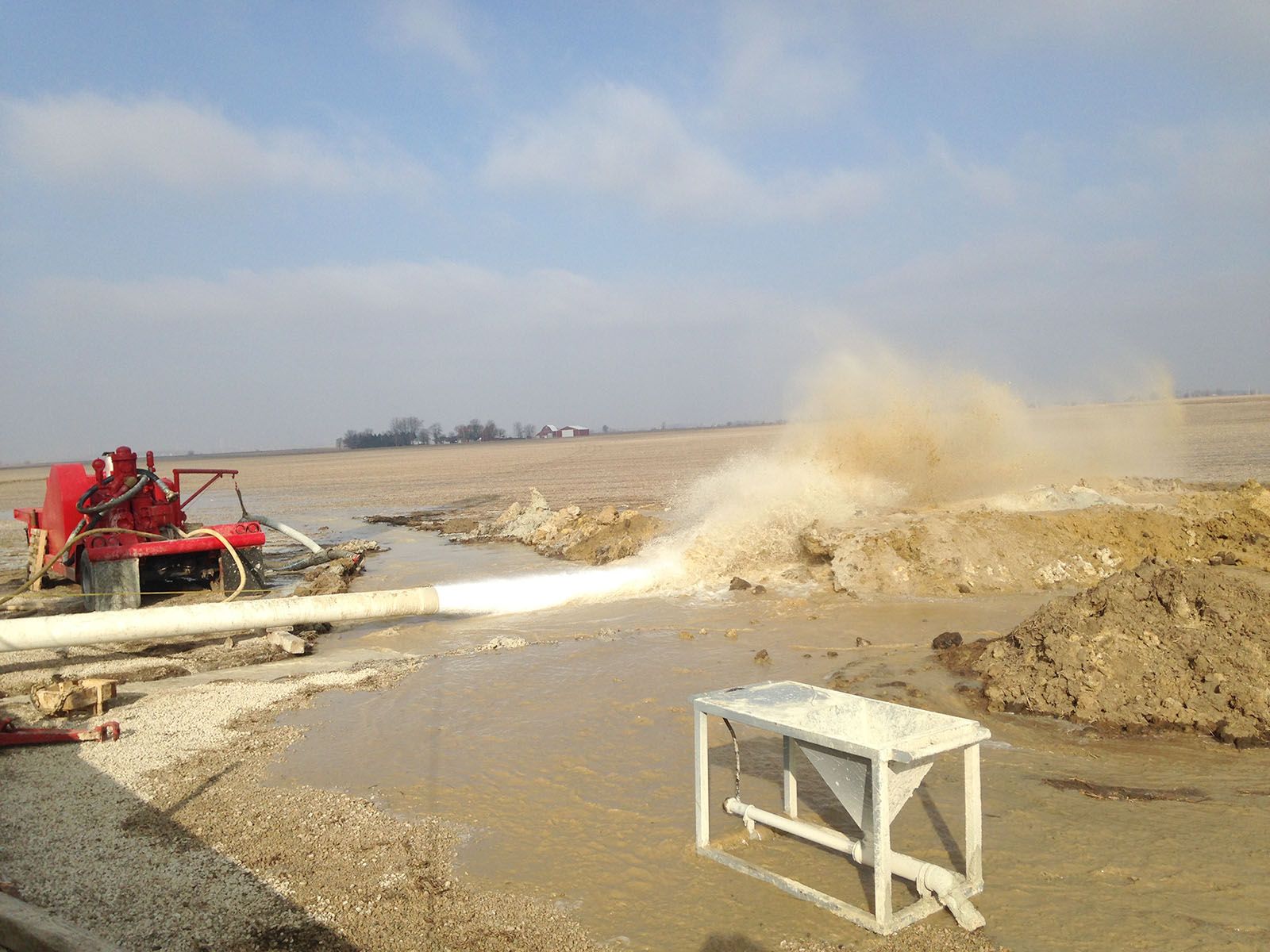 A drilling rig pumping water across a muddy construction site
