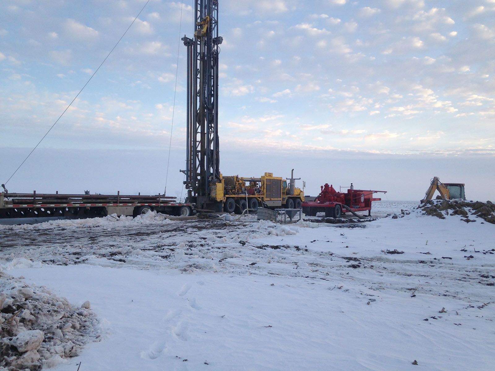 Snow-covered construction site with a tall drilling rig and heavy machinery