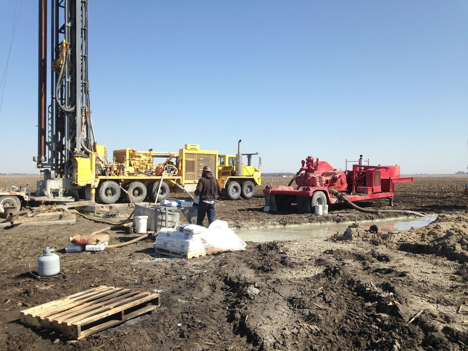 Drilling rig and heavy trucks at a muddy construction site