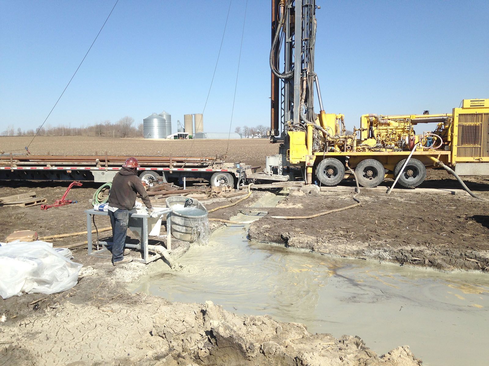 Construction site with drilling rig, muddy water, and worker near equipment