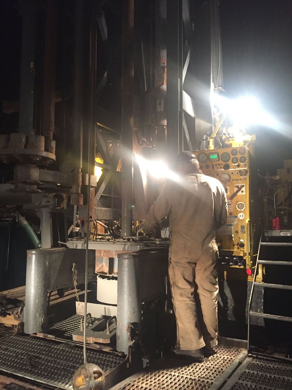 Worker inspecting machinery in a dim industrial facility, lit by bright work lights.