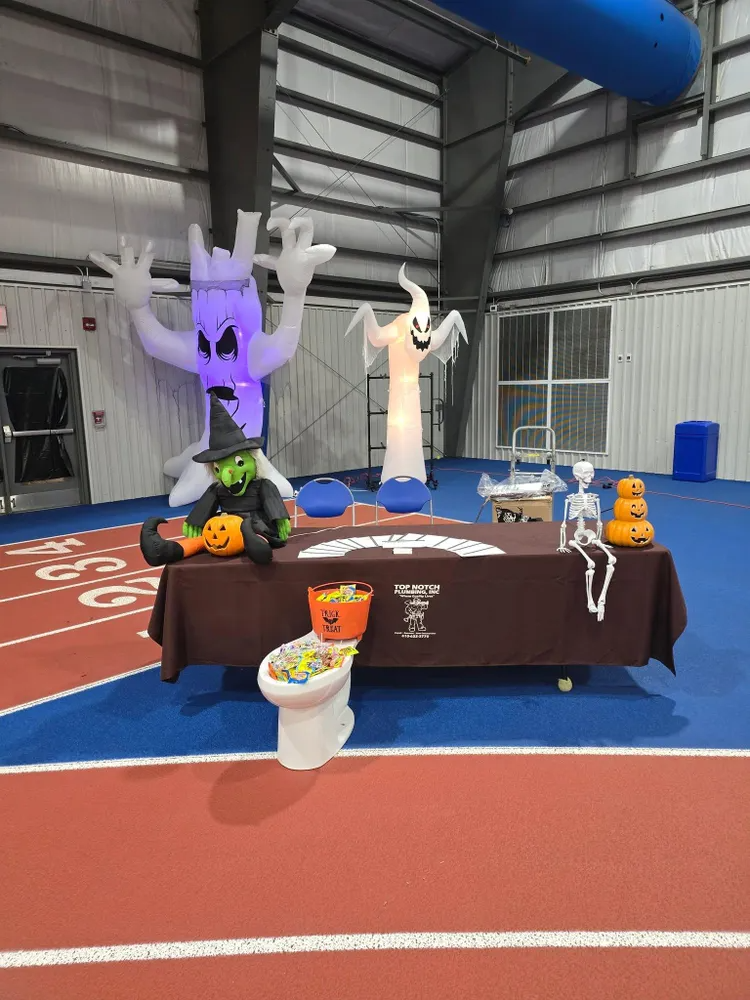 A Halloween display with inflatable ghosts, a witch, skeleton, and a toilet full of candy on a table at an indoor track.