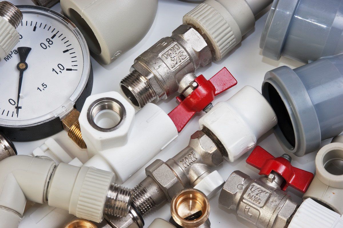 Assorted plumbing fittings, valves, and a gauge scattered on a white surface