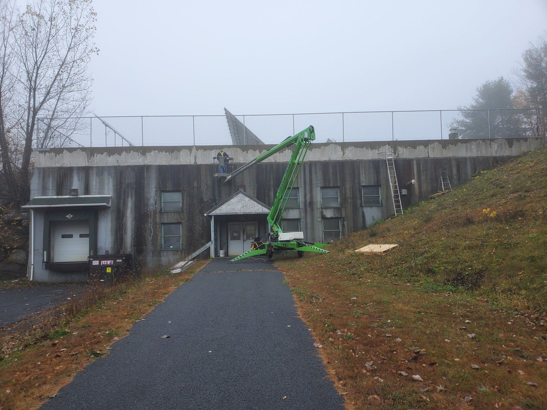 A green crane is sitting in front of a building on a foggy day.