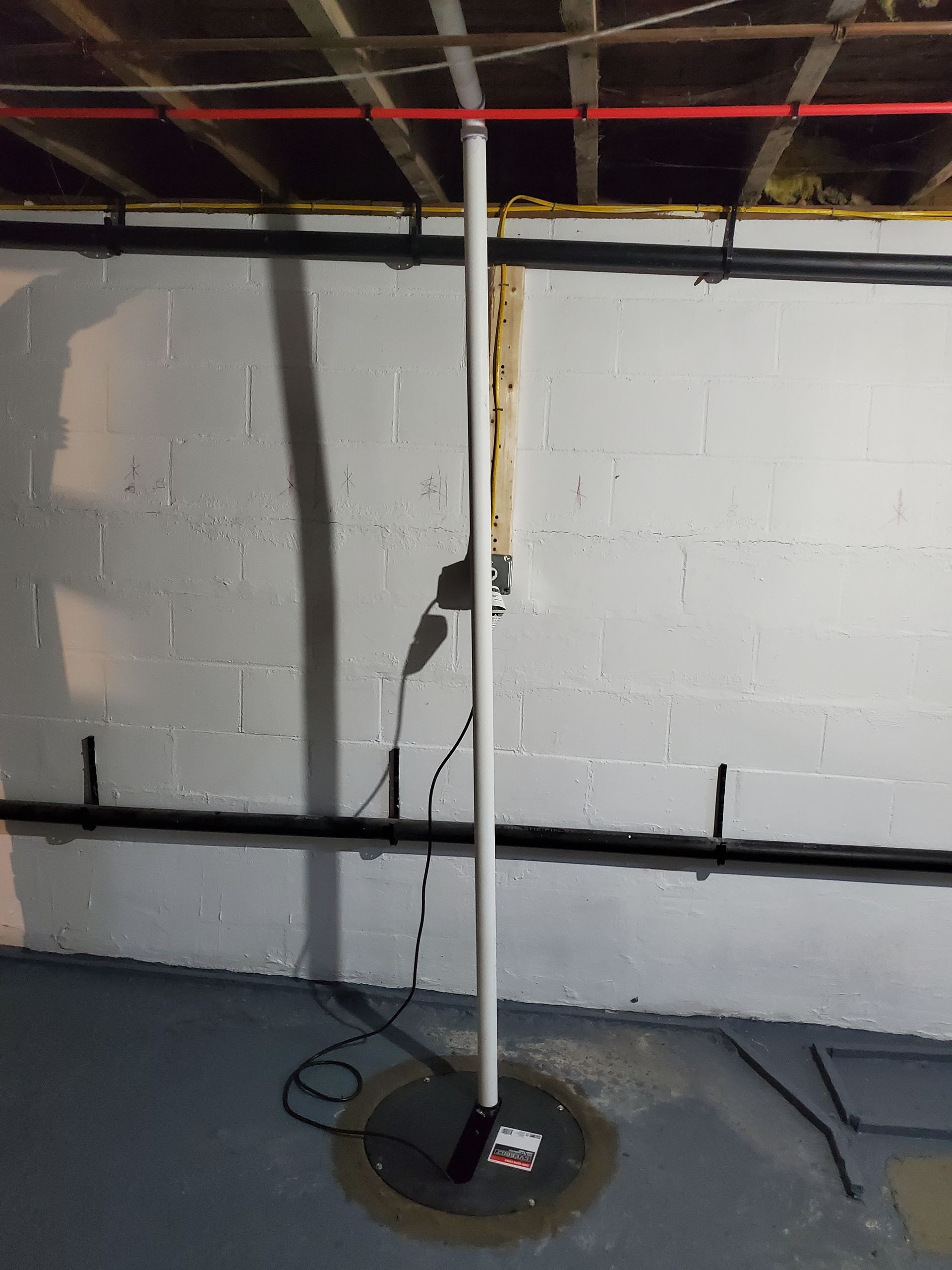 A white pole in a basement next to a brick wall