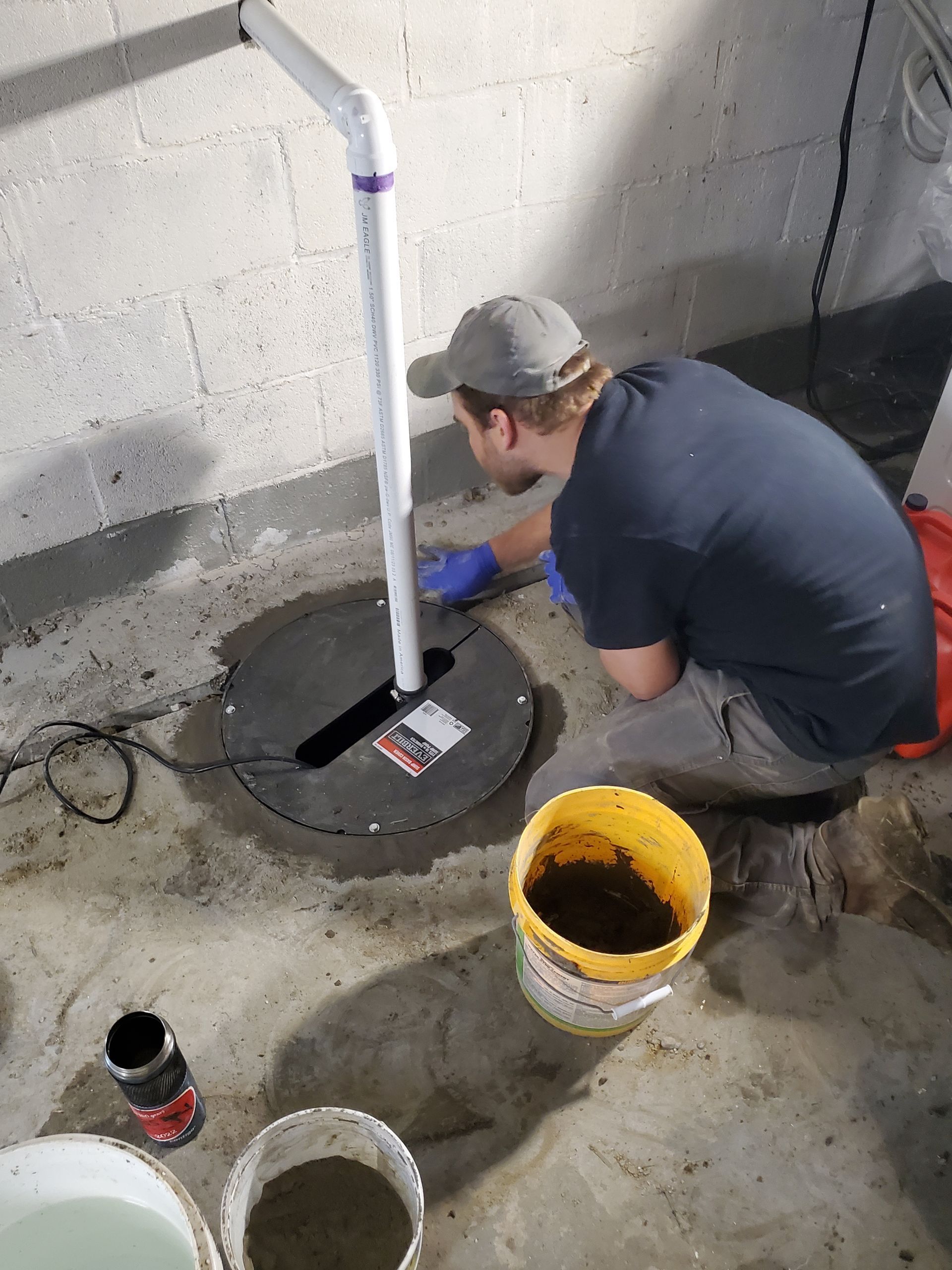 A man is working on a sump pump in a basement.