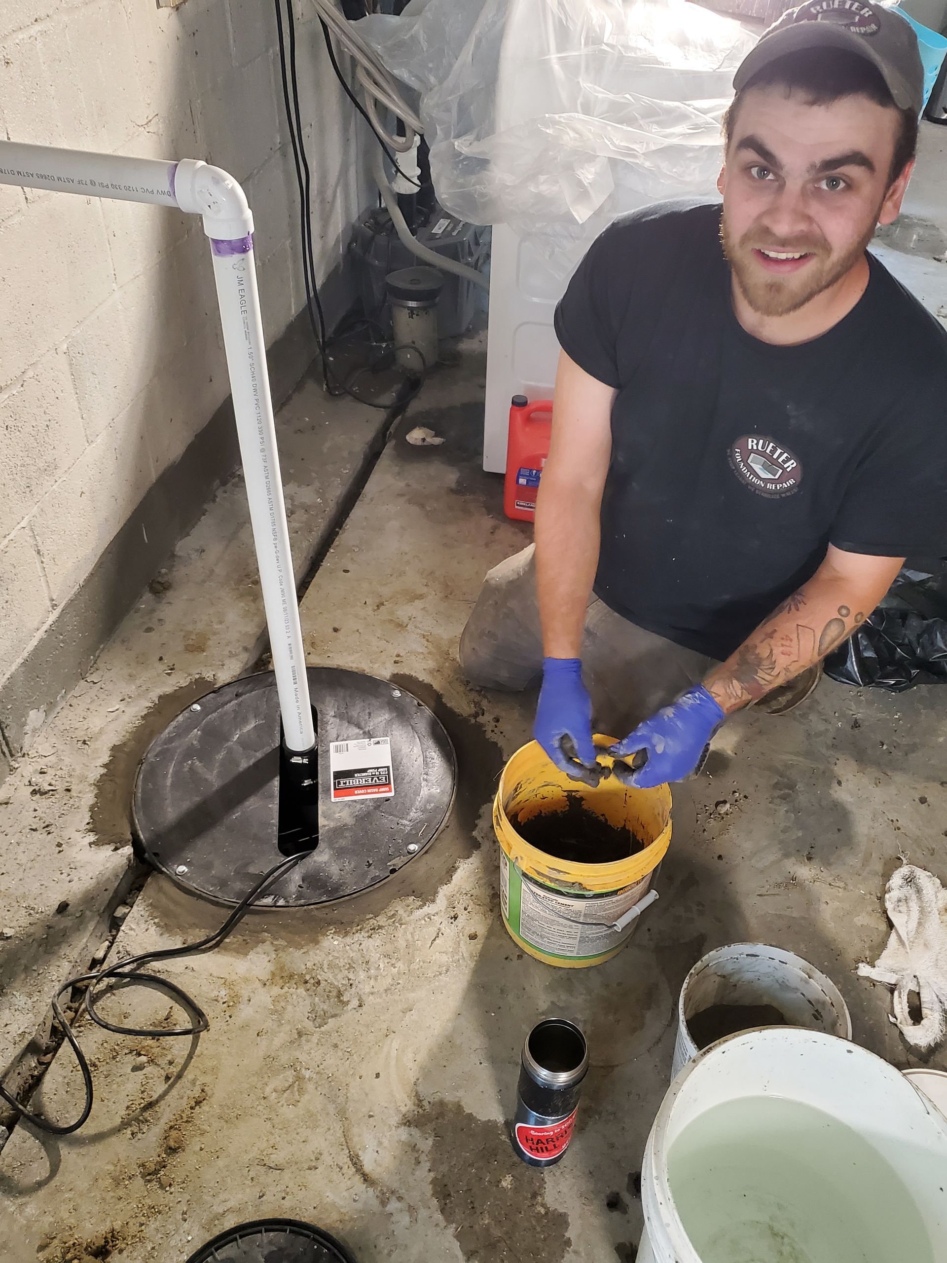 A man is kneeling down next to a bucket of water in a basement.