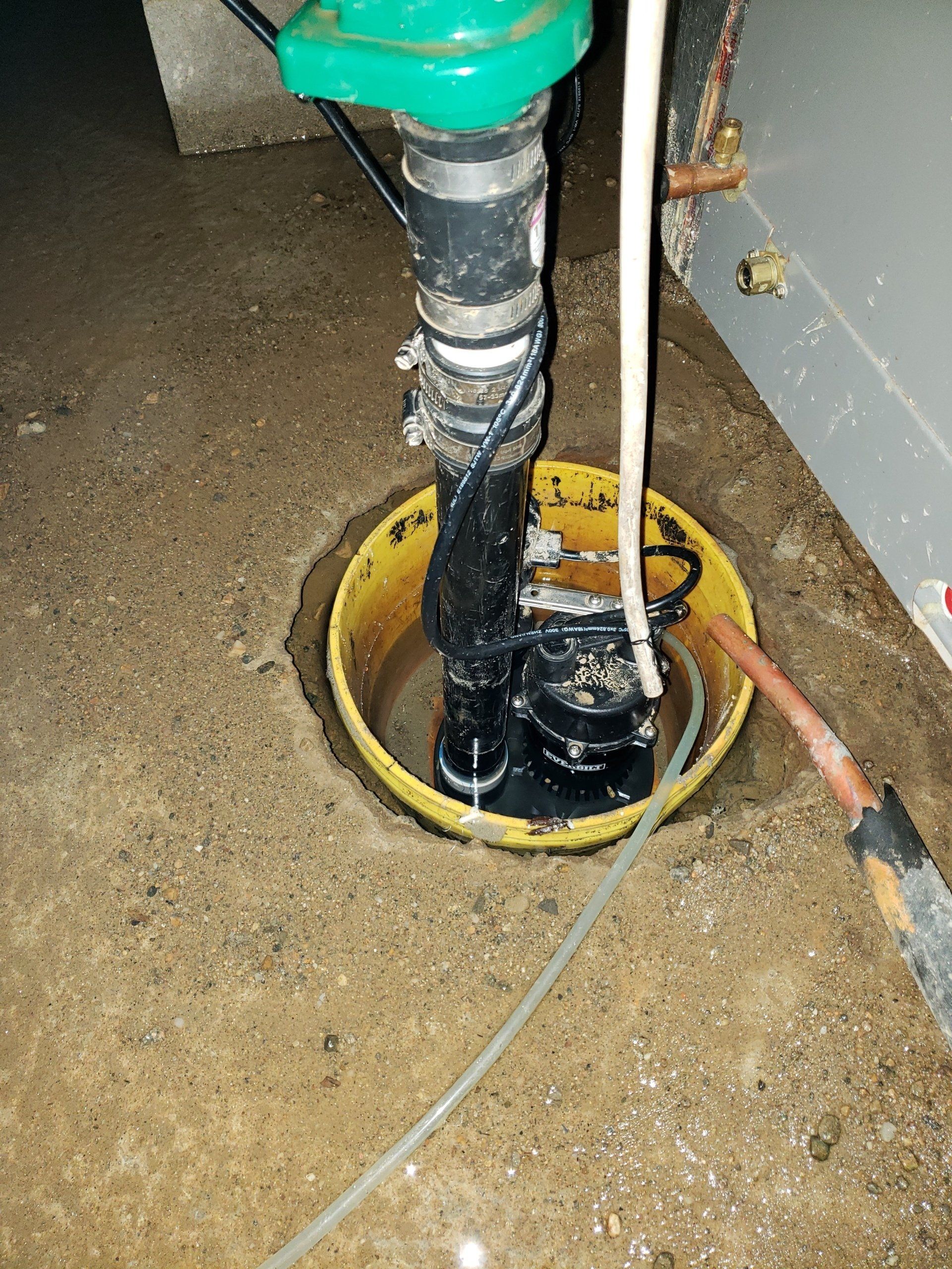 A sump pump in a basement with a hose attached to it.