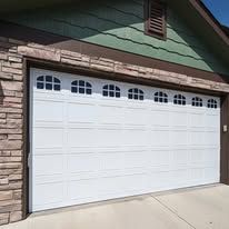 White garage door with decorative arched windows on a green house exterior