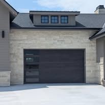 Modern stone house exterior with a dark garage door and white driveway
