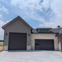 Modern gray house exterior with two large garage doors and a concrete driveway under a partly cloudy sky