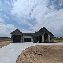 New gray single-story house with three-car garage and unfinished dirt front yard under cloudy sky