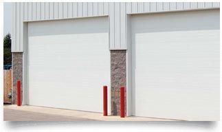 Two white industrial garage doors on a metal building with red bollards in front