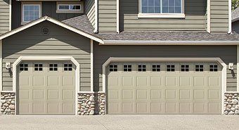 Two beige garage doors on a gray house with stone accents and windows above