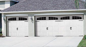 Two white garage doors on a gray suburban house with a concrete driveway
