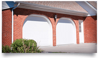 Brick garage with two white doors, brick arches, and a small bush by the driveway
