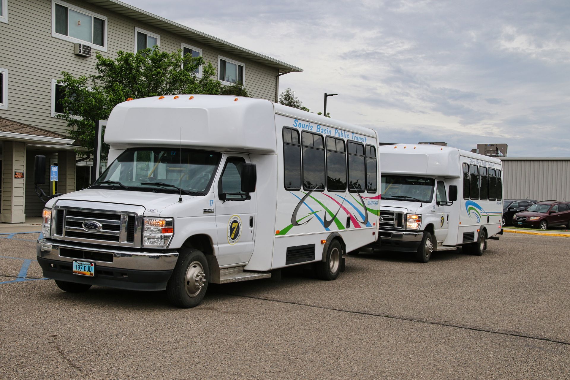 Two white buses are parked in front of a building.