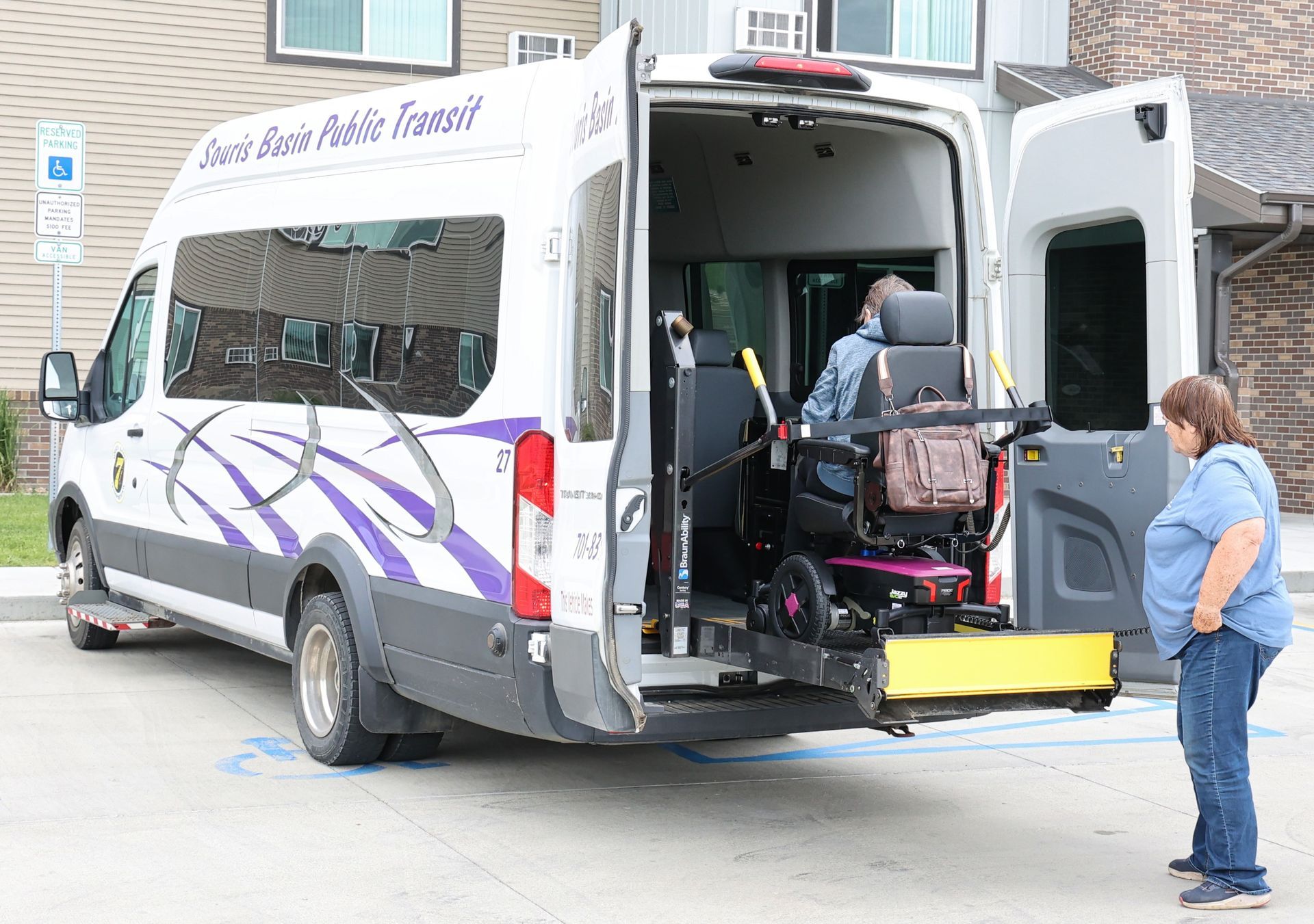 Van with ramp lowered for wheelchair; woman watches. Exterior, daytime.