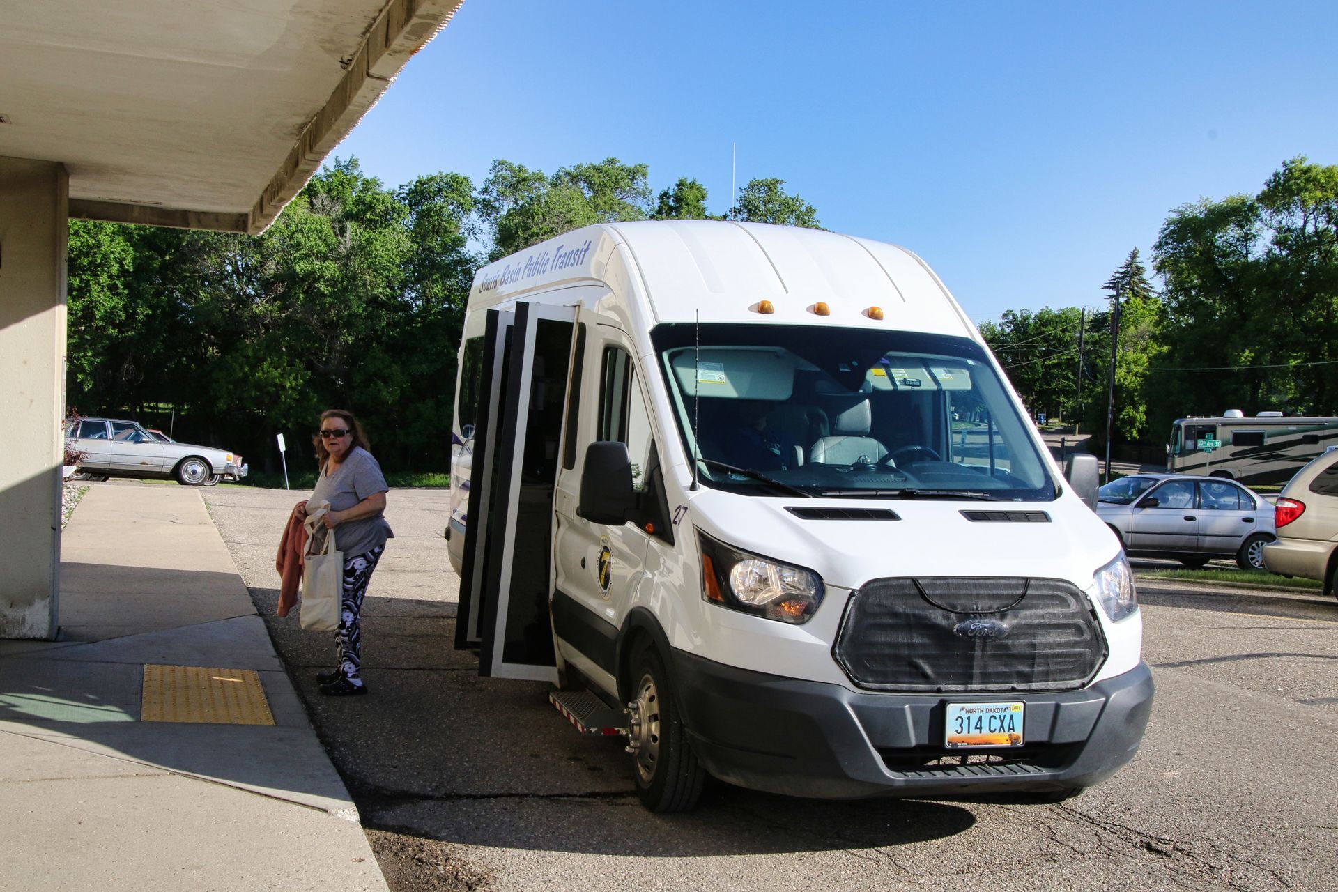 A white van is parked in a parking lot with a woman standing next to it.