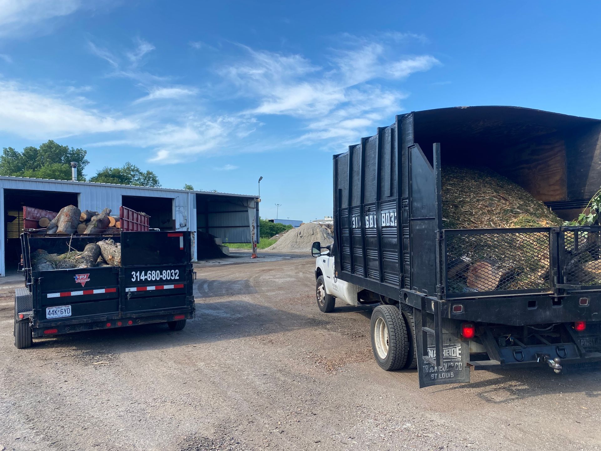 Two trucks loaded with hay bales parked on a gravel farm lot under a blue sky