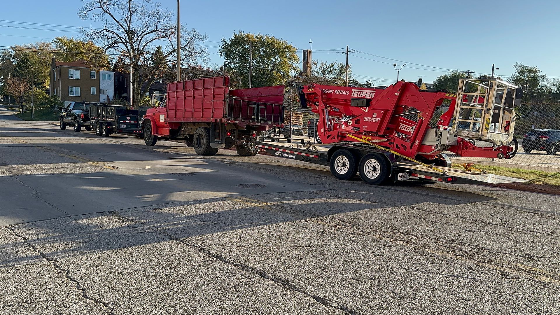 Red and black industrial trailers parked on a gravel lot under trees in daylight