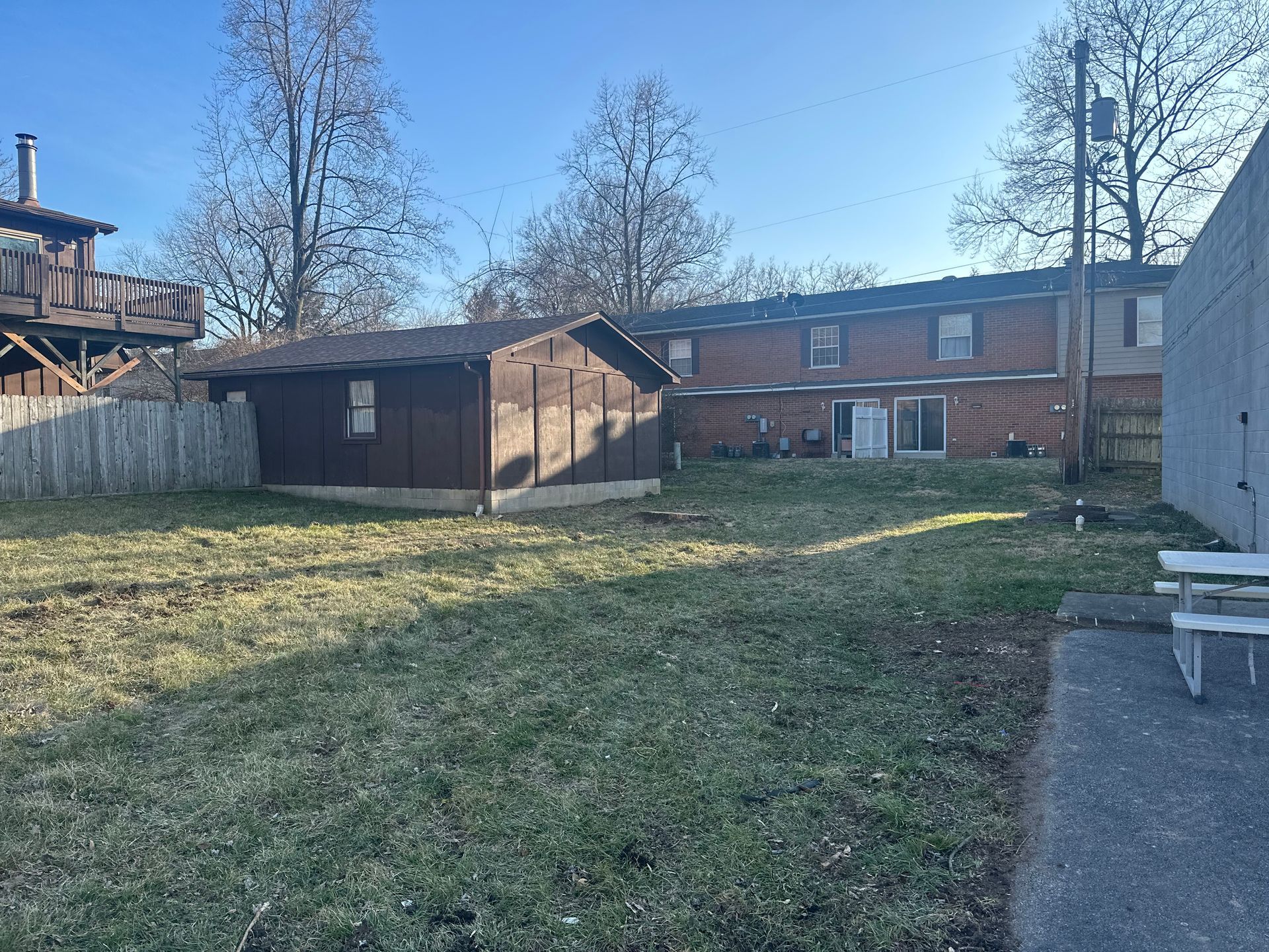 Backyard with grass, shed, brick houses, and clear blue sky