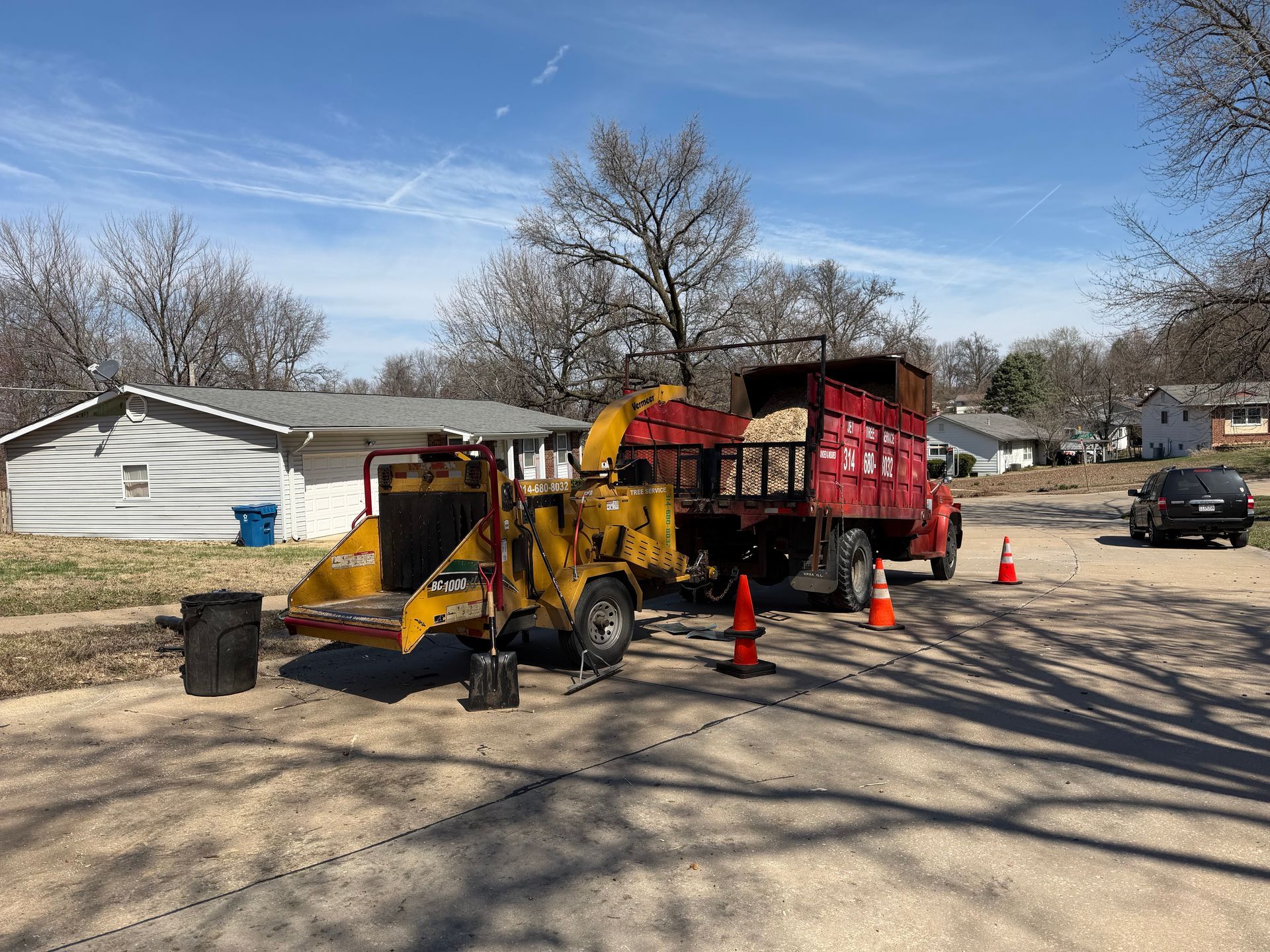 Yellow loader and red dump truck on a residential street with traffic cones and debris cleanup underway