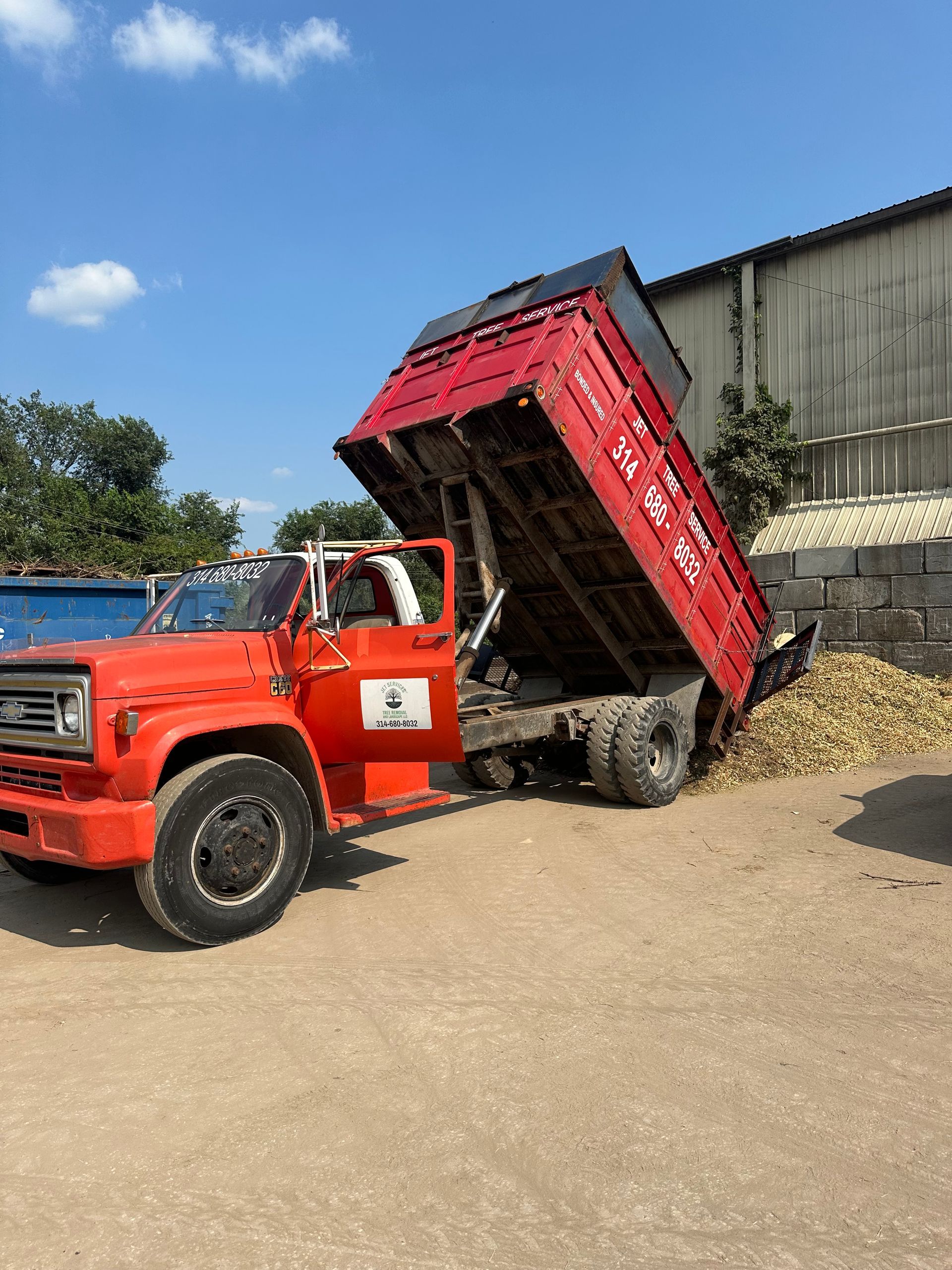 Red dump truck tipping bed raised high while unloading gravel in a yard