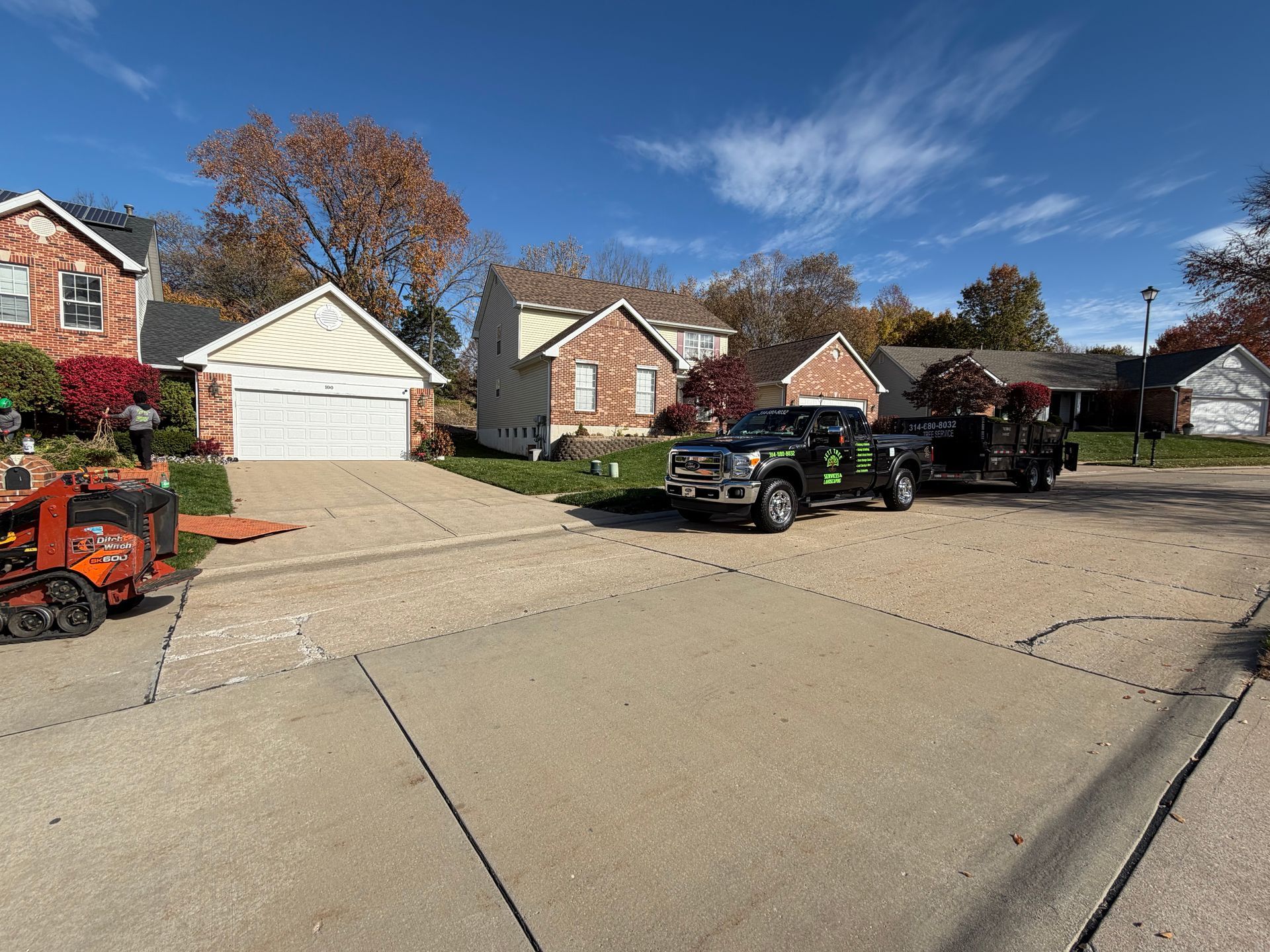 Suburban street with brick houses, parked utility trucks, and a garage on a sunny day