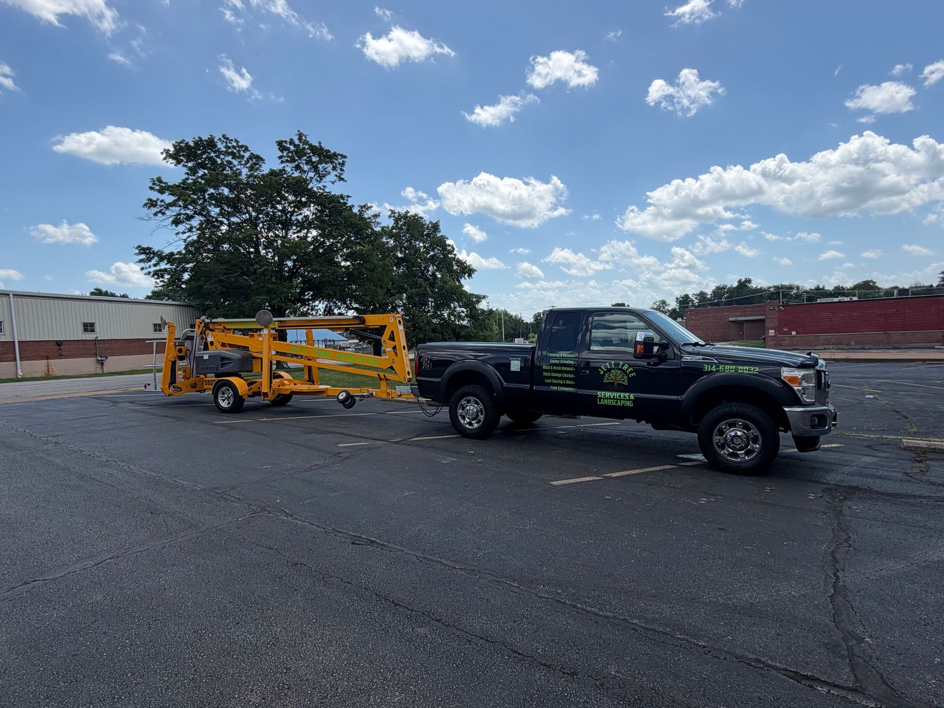 Tow truck hauling a black pickup truck in a parking lot under a blue sky with clouds