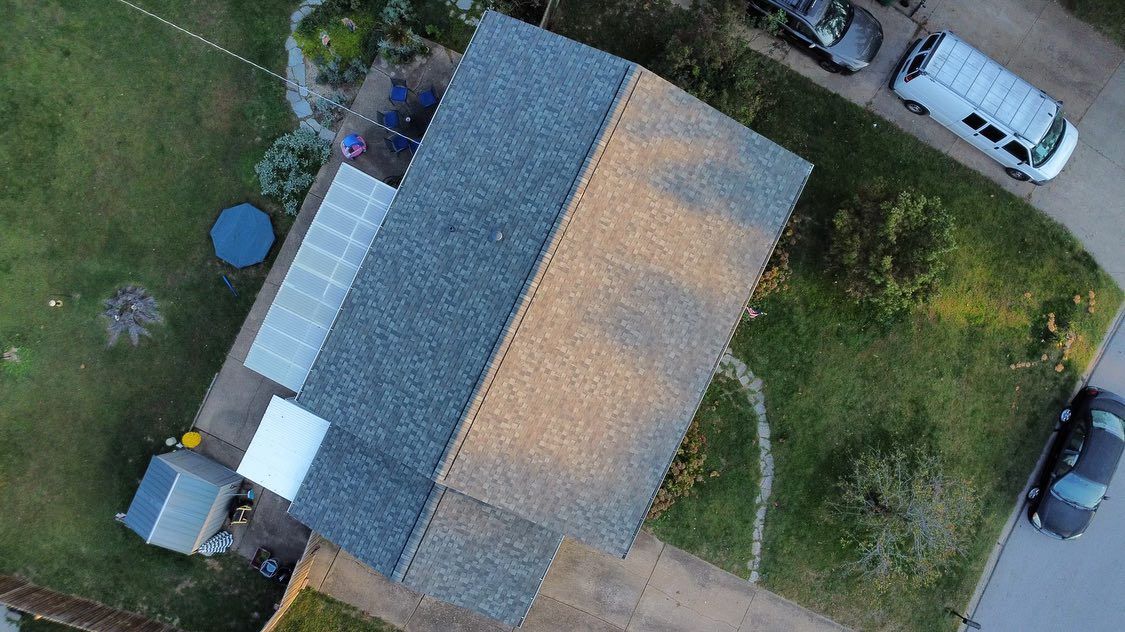 Overhead view of a house with a gray roof, green lawn, and parked vehicles on a driveway.