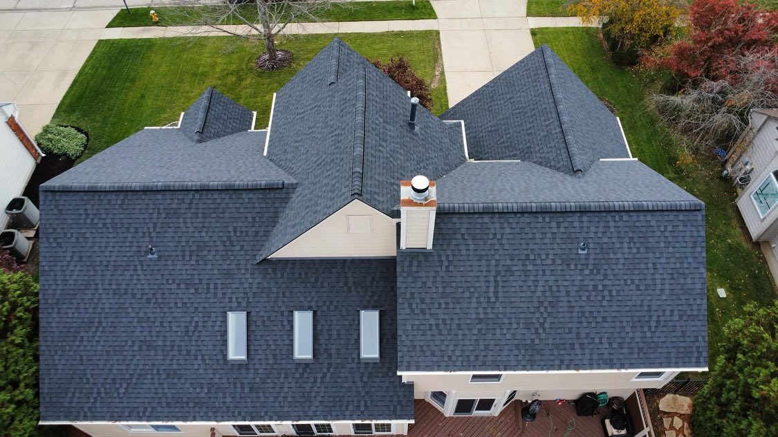 Overhead view of a house with a dark gray shingled roof, a chimney, and three skylights.
