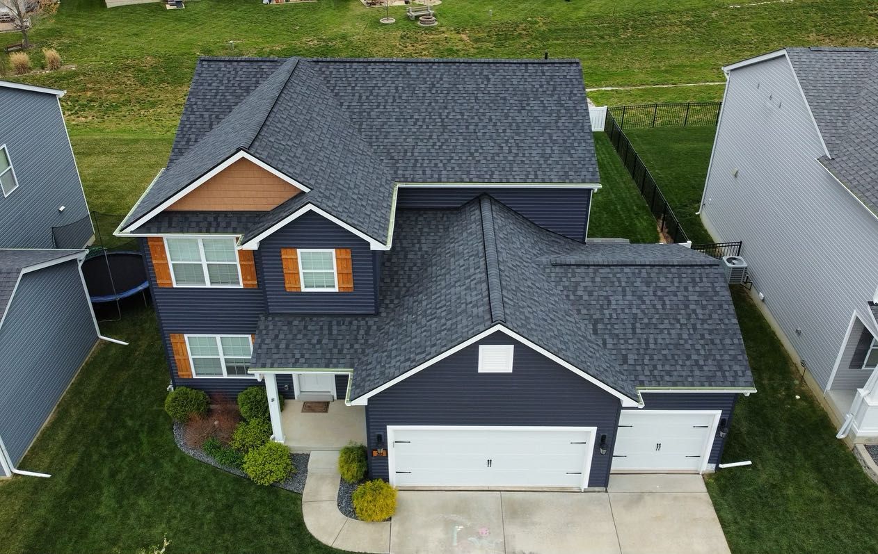 Dark blue house with black roof, brown shutters, and a white garage door, aerial view.