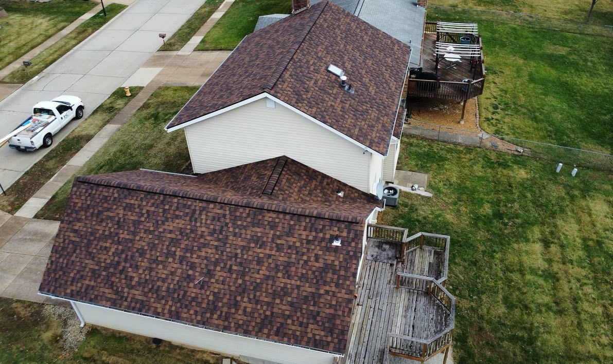 Overhead view of a house with a brown shingled roof, a white exterior, and a wooden deck. A truck is parked on the street.