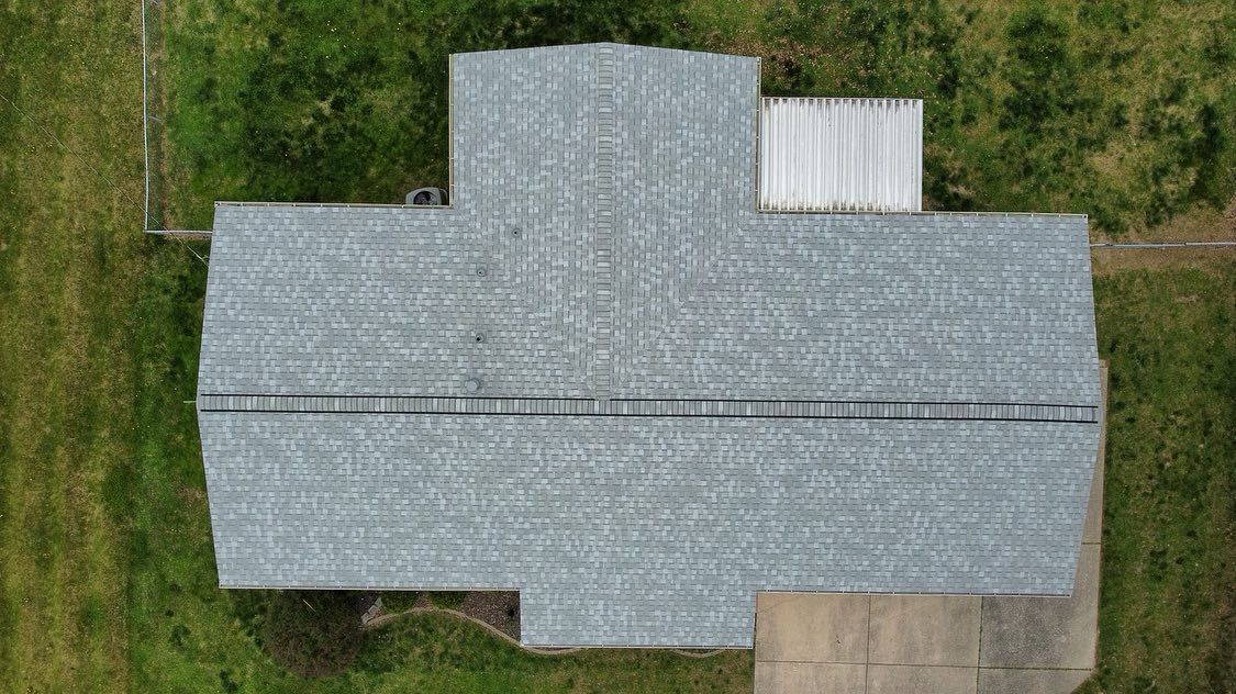 Overhead view of a gray-shingled roof on a house, small white roof to the right, green lawn.