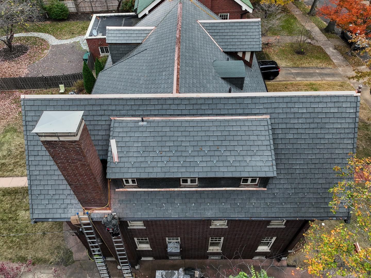 Overhead view of a brick house with a dark gray shingled roof, a chimney, and a small dormer.