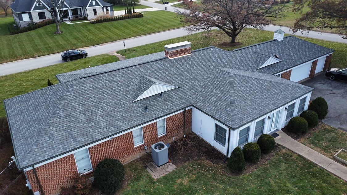 Aerial view of a one-story brick and white-walled building with a gray roof and surrounding green grass.