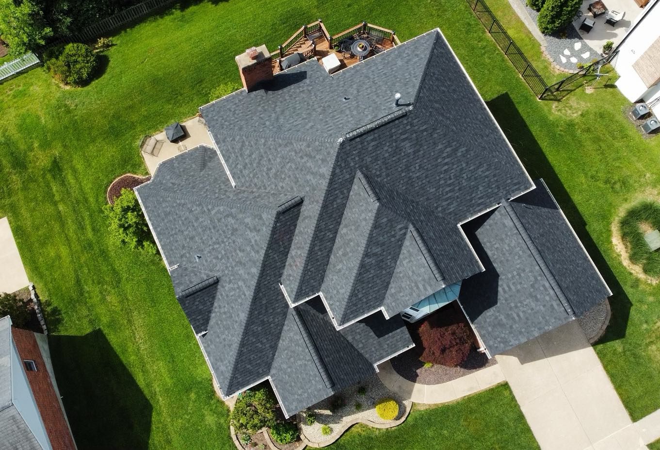 Aerial view of a dark gray shingled roof on a house surrounded by green grass.