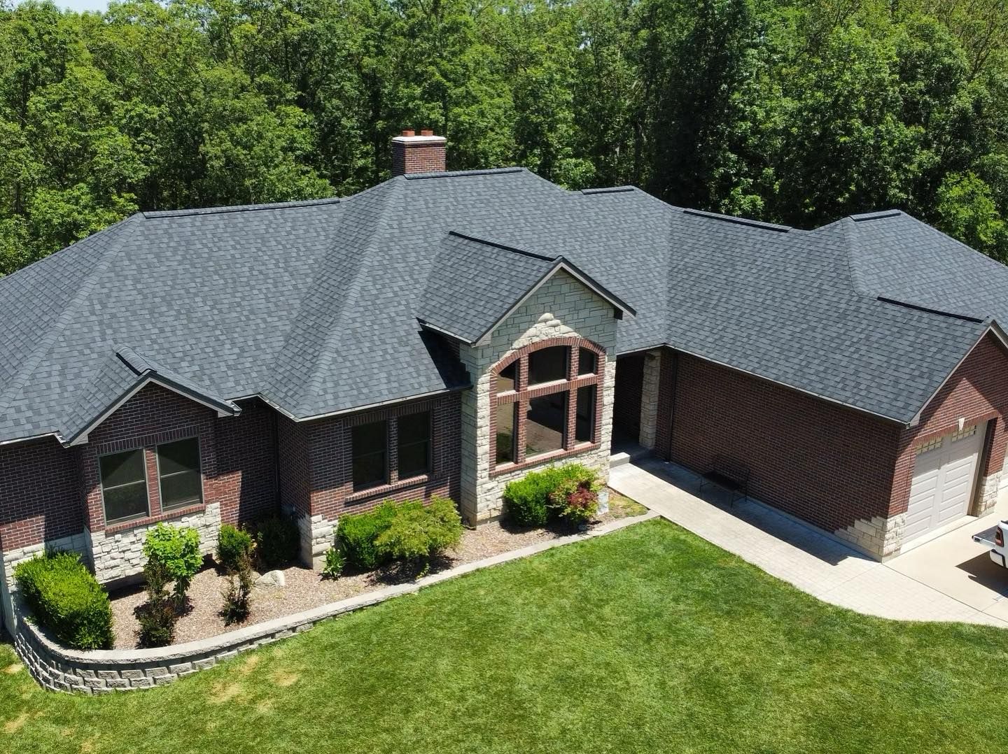 House with dark gray roof, brown siding, stone accents, and green lawn.