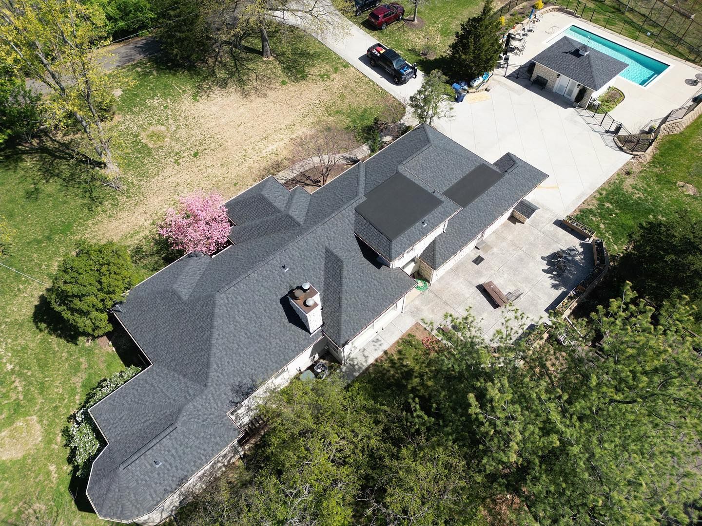 Aerial view of a house with a dark roof, pool, and surrounding green landscape.