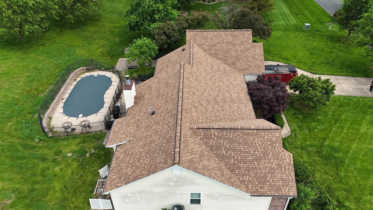 Overhead view of a house with a brown roof, surrounded by green grass and a pool covered in a dark blue tarp.