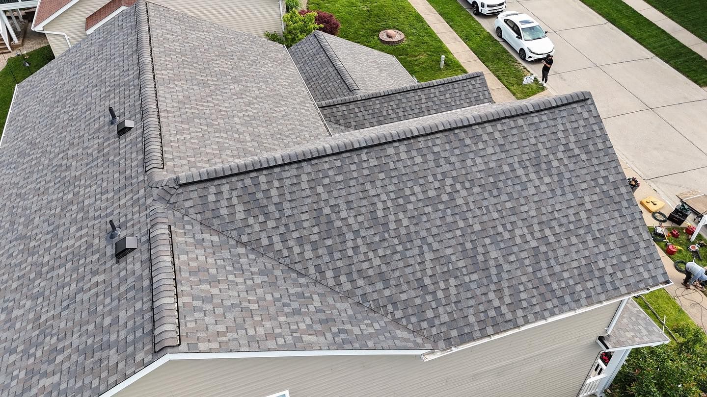Overhead view of a house roof with gray shingles. A street and green lawn are in the background.